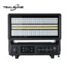 A black electronic device labeled TEALSHINE, featuring a rectangular grill, control knobs, buttons, and a display screen on its front panel—likely an amplifier or heater—sits beside an IP65 Mini 1176 Moving Strobe Light that adds dynamic illumination to its surroundings.