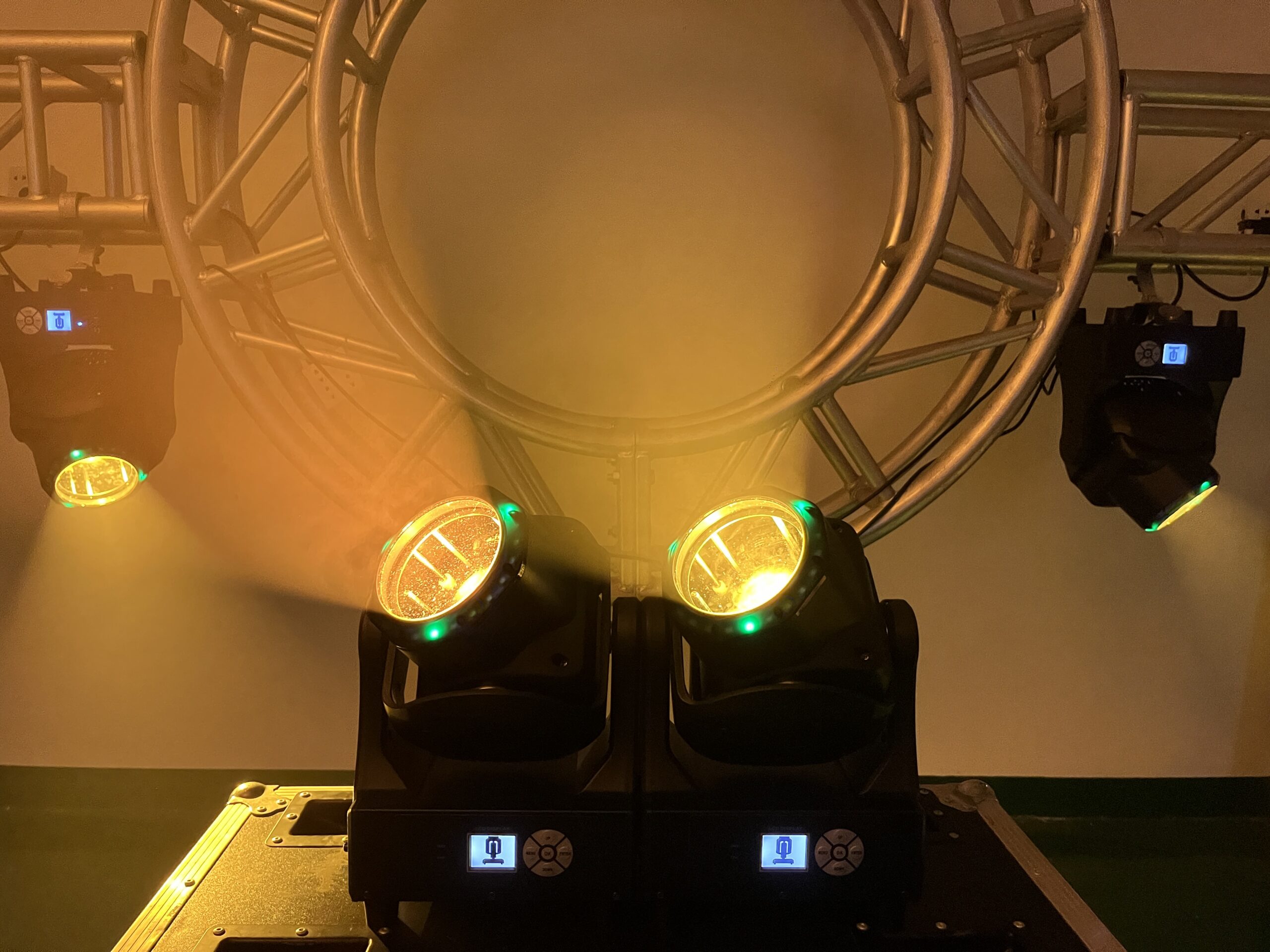 IP20 150W Led Beam Wash Moving Head Lights 2 Two IP20 150W LED Beam Wash Moving Head Lights emit bright yellow beams, providing vivid illumination, while an additional beam wash light adds depth to the lighting design. A circular metal truss and two more lights glow in the background, enhancing the scene’s dynamic atmosphere for a performance or event.