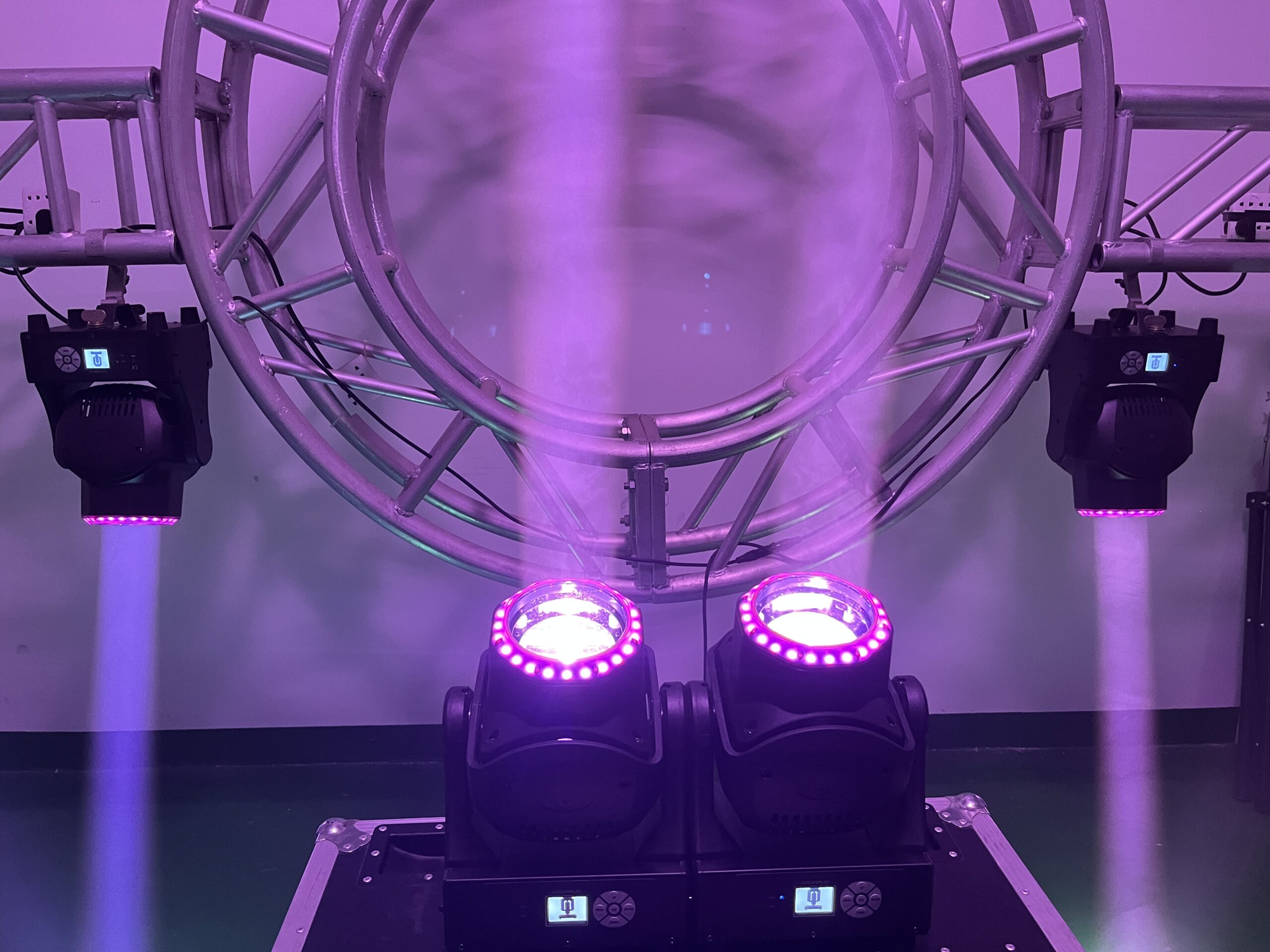 IP20 150W Led Beam Wash Moving Head Lights 3 Two IP20 150W LED Beam Wash Moving Head Lights emit purple beams upward, positioned in front of a circular metal truss fitted with additional mounted beam wash lights. The background is plain, and the setup appears ready for a light show or event.
